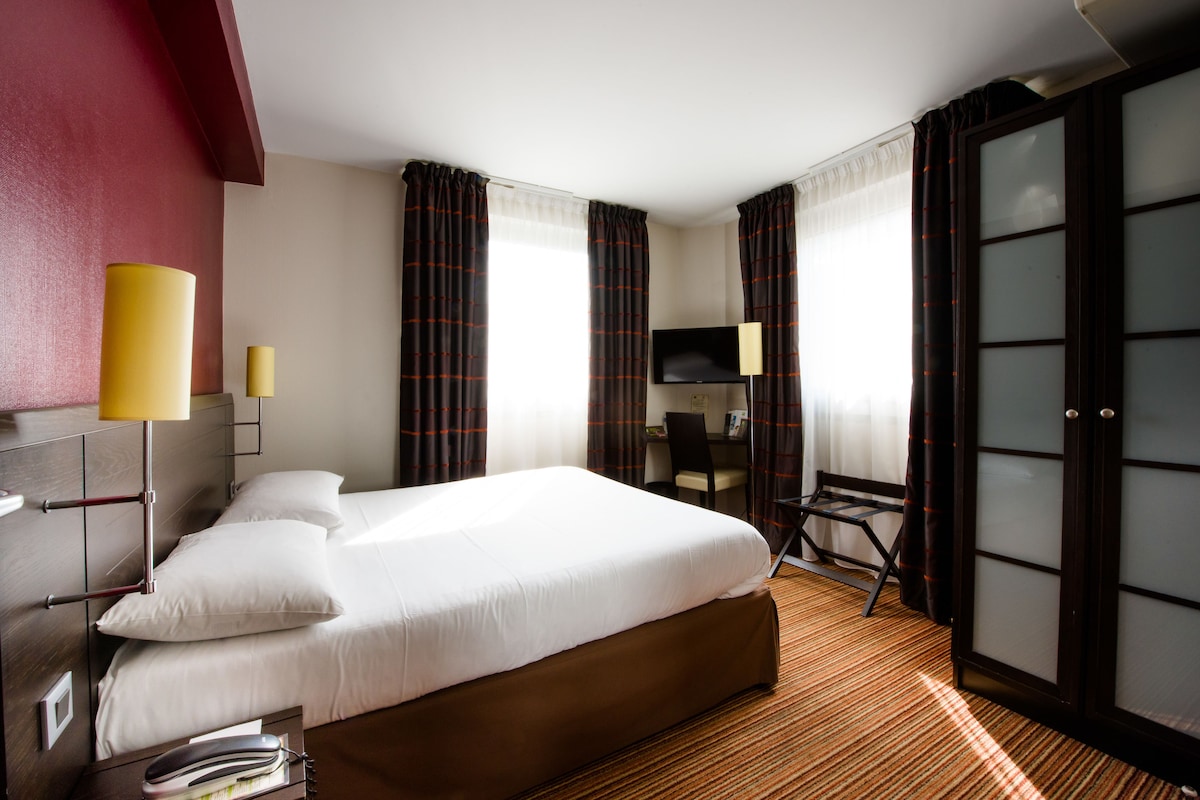 Une chambre d’hôtel avec un grand lit, un bureau, une chaise, une télévision et une porte coulissante.