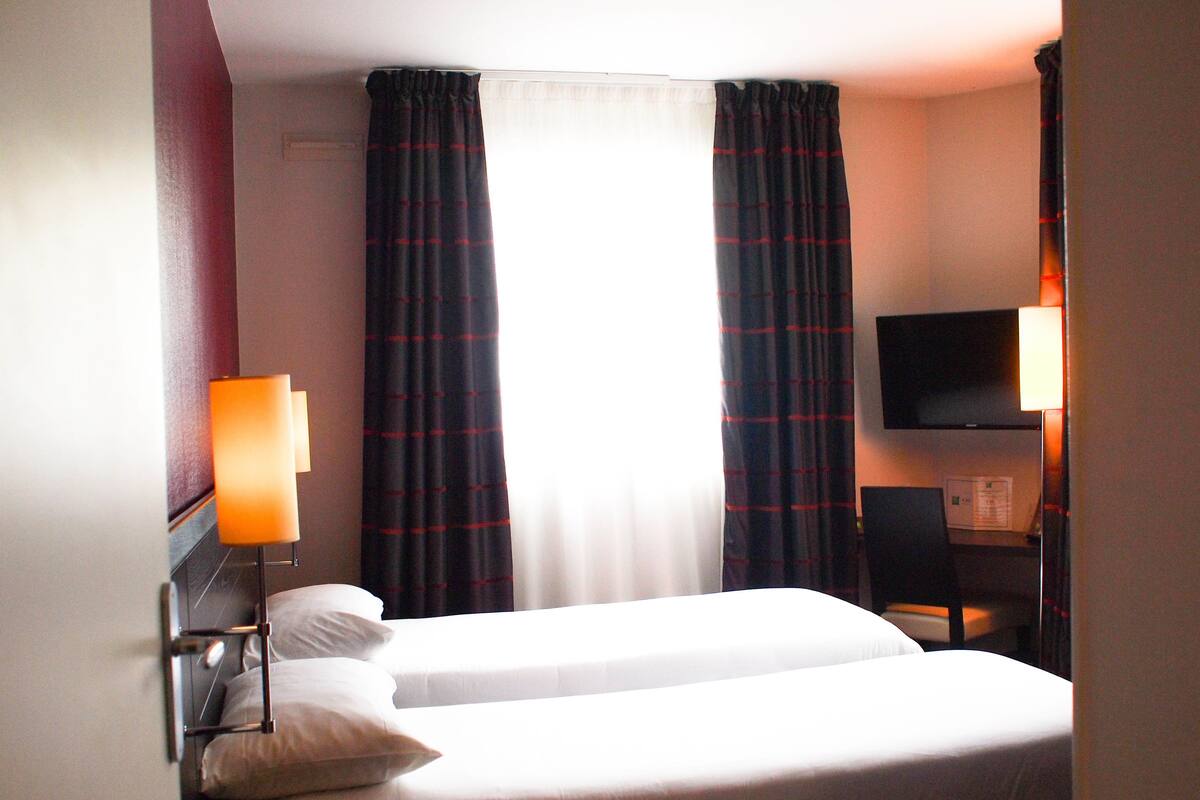 Une chambre d’hôtel avec un lit, deux lampes de chevet, une télévision et un bureau avec une chaise.