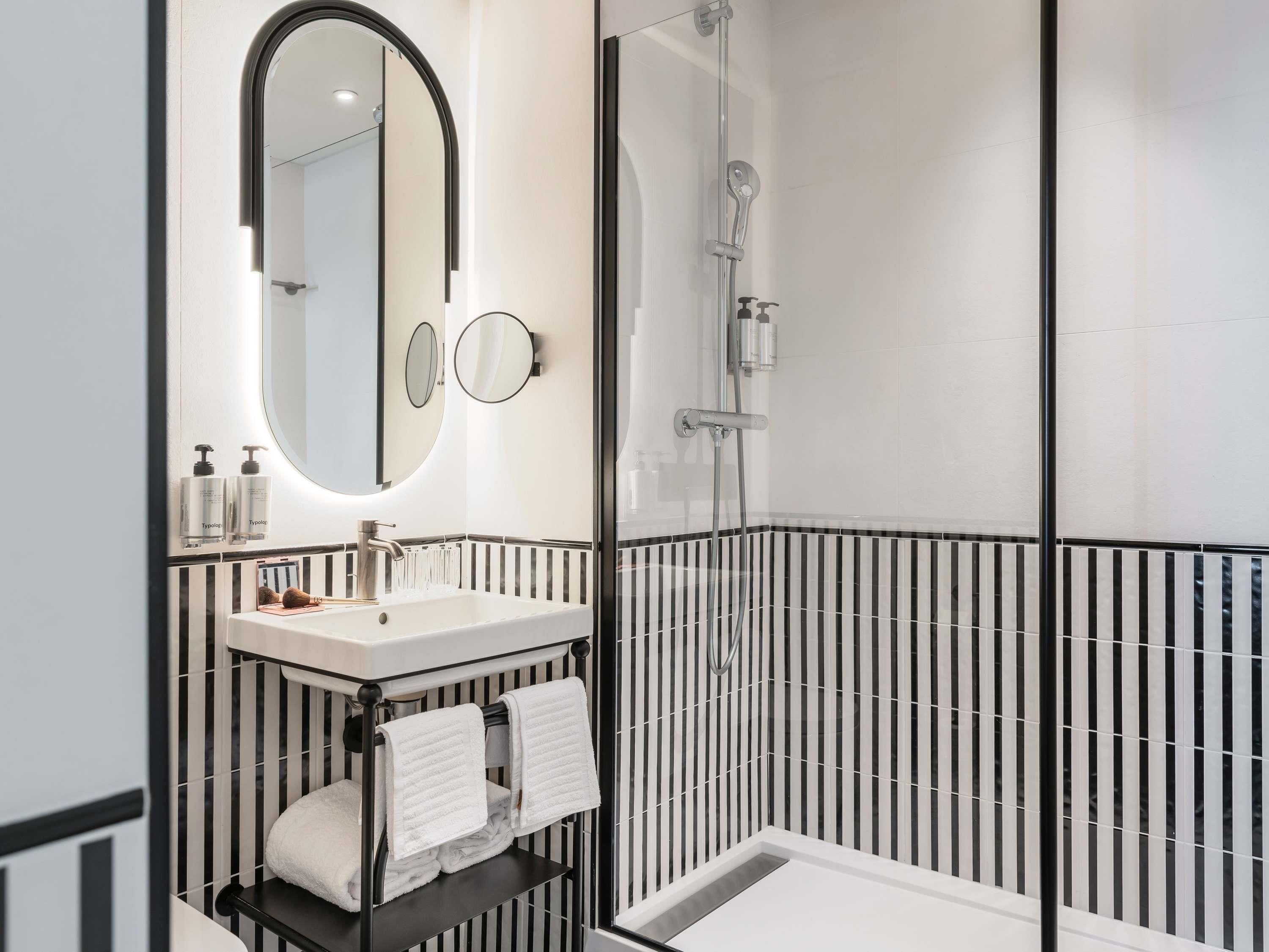 Ein modernes Badezimmer mit einer gläsernen Duschkabine, einem weißen Waschbecken und einer schwarzen Arbeitsplatte sowie zwei Spiegeln.