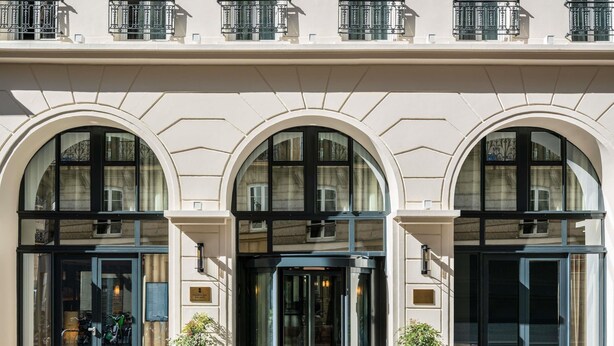 L’entrée d’un hôtel, avec trois fenêtres en arc de cercle, une porte en verre et une petite plante en pot placée devant.