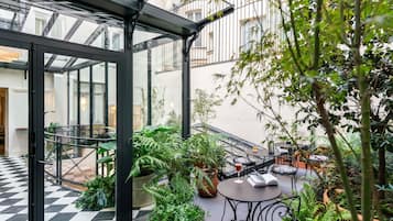 Un patio exterior moderno con paredes de vidrio, plantas en macetas y mobiliario para exteriores.