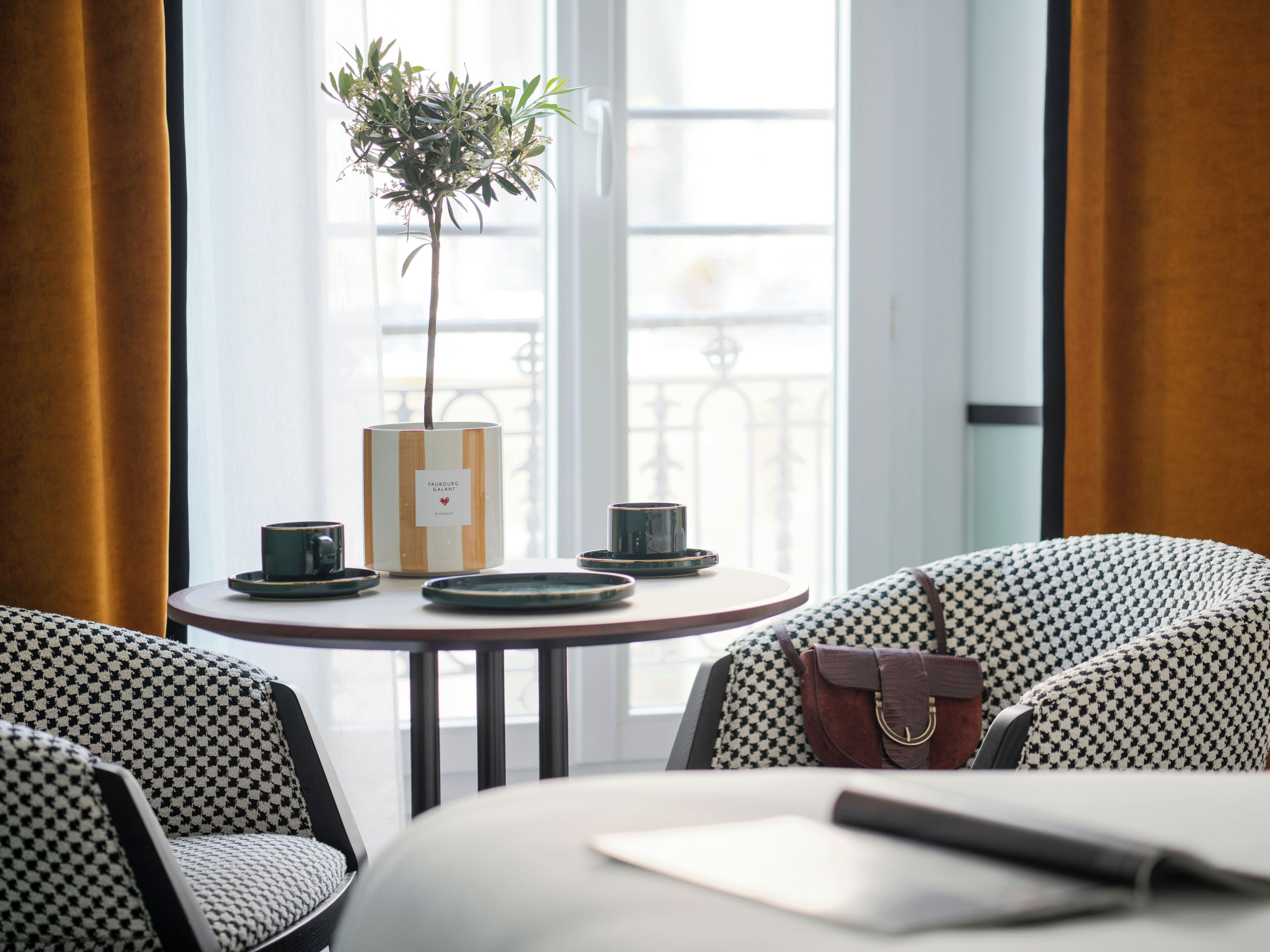 Een tafel met een bloemenvaas, een kopje en een bord, in een kamer met gestreepte stoelen en uitzicht op een balkon.
