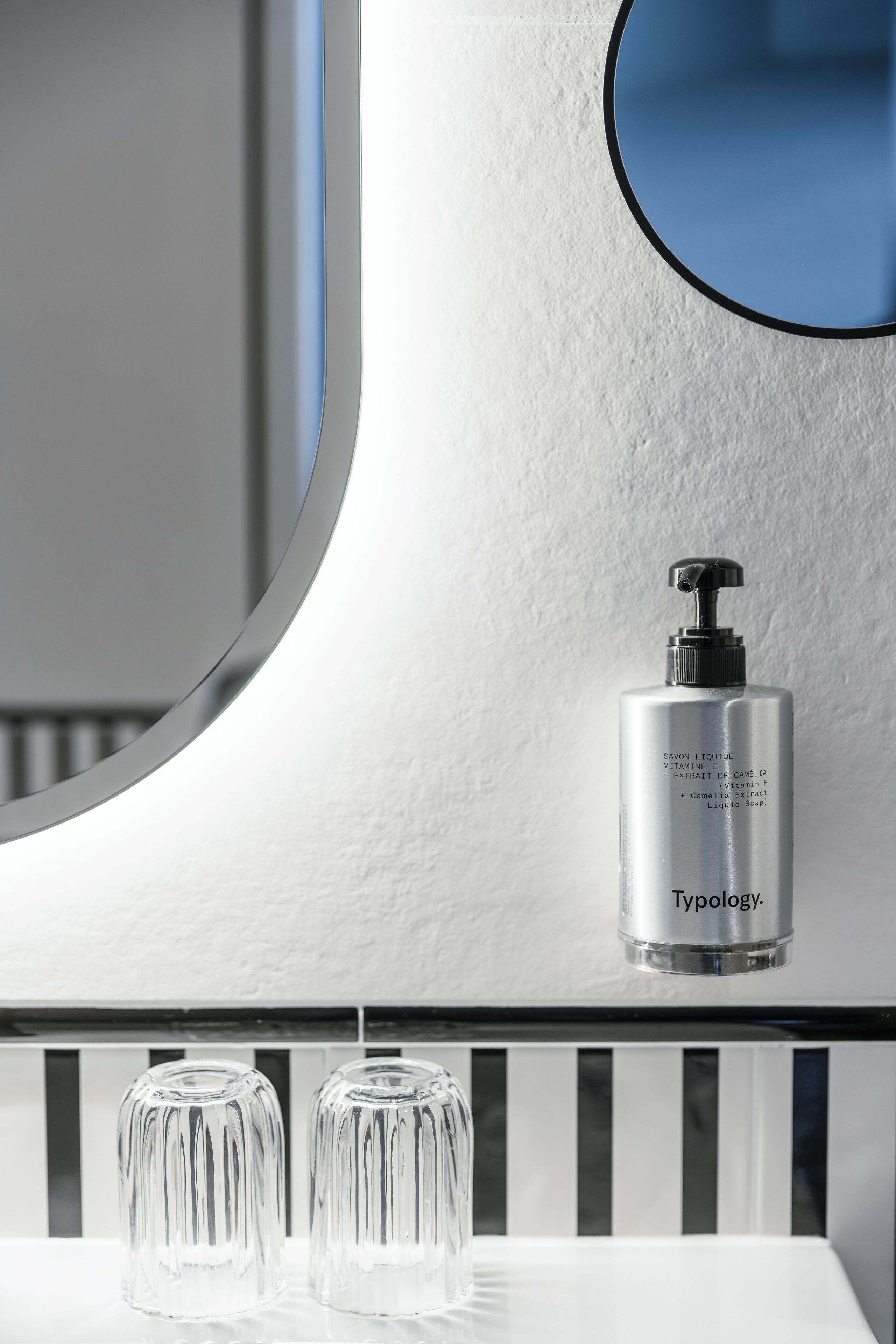 A bathroom with a white sink, a mirror, and a bottle of Typology liquid soap.