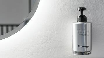 A bathroom with a white sink, a mirror, and a bottle of Typology liquid soap.