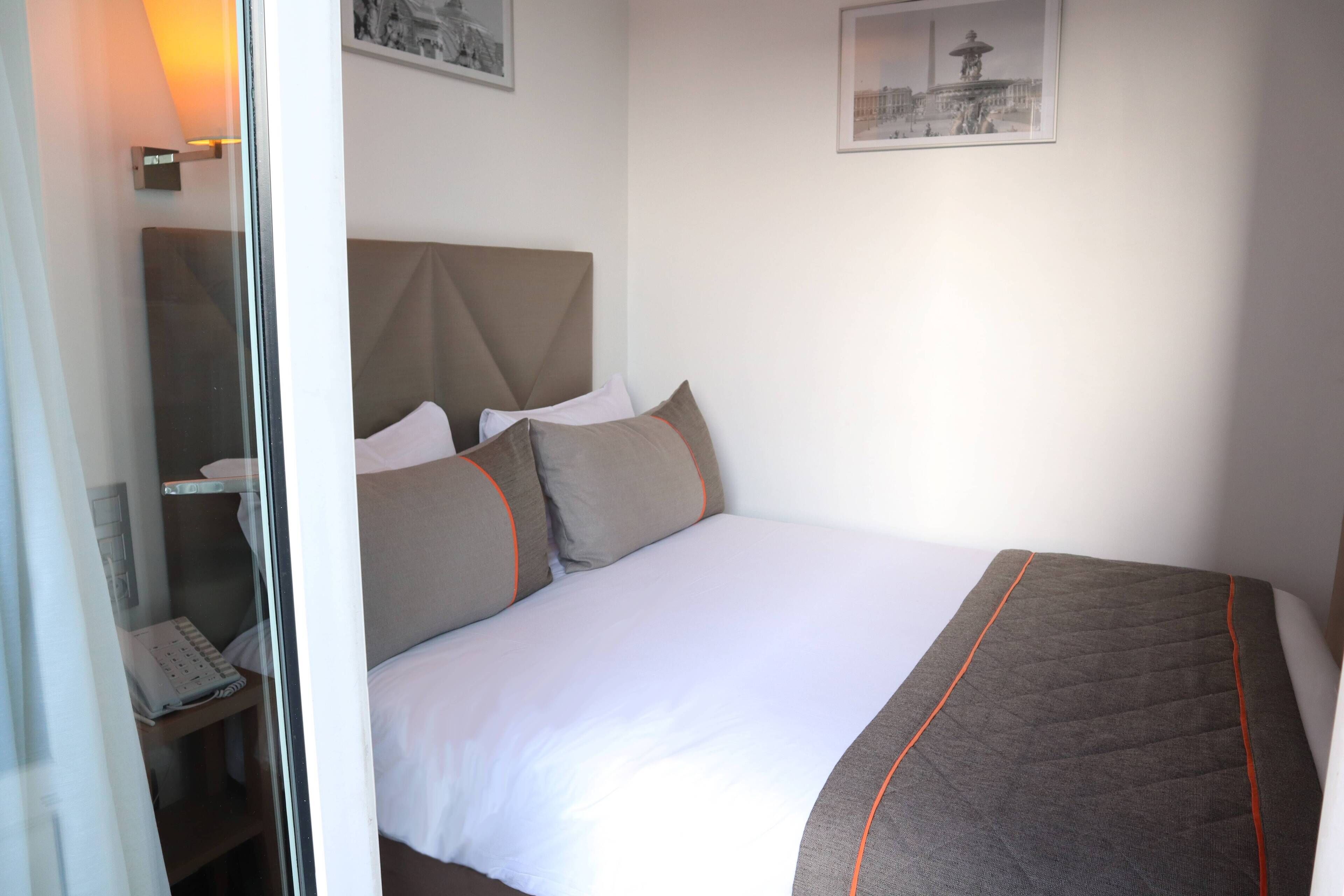 A hotel room with a bed, a bedside table with a lamp, and a wall-mounted picture.