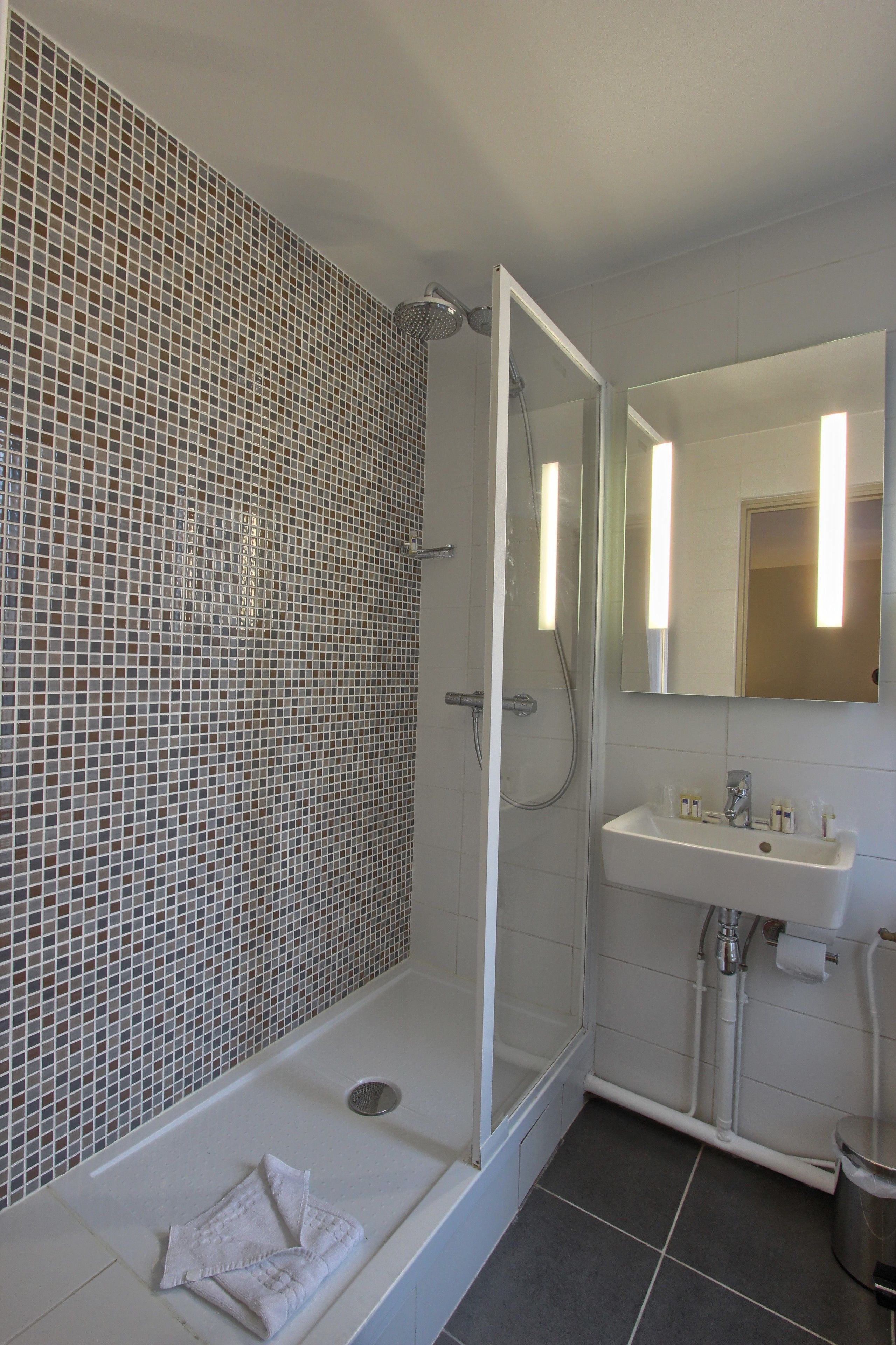 A modern bathroom with a glass-enclosed shower, a white sink, and a tiled mosaic wall.