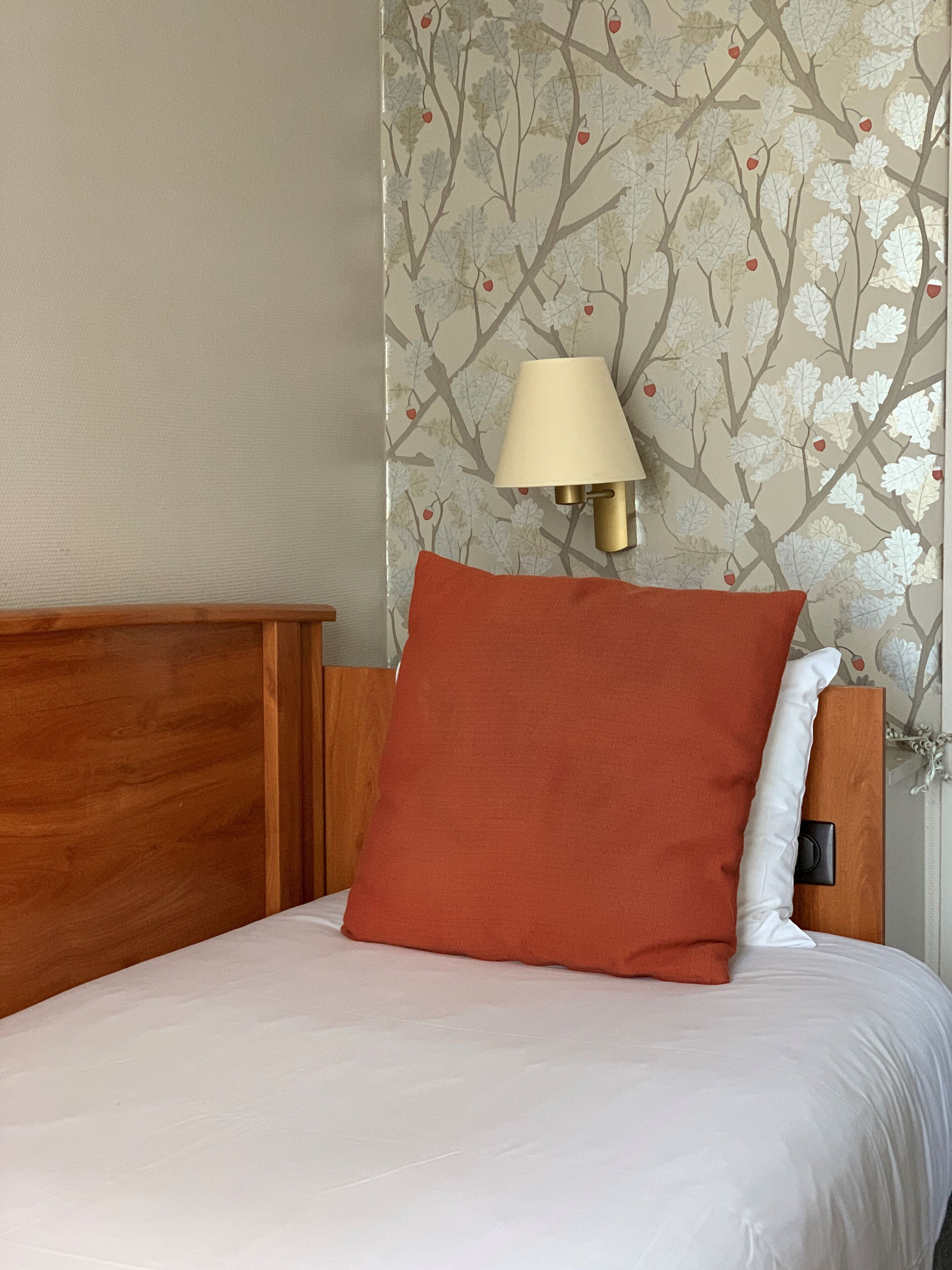 A bed with a wooden headboard, a red pillow, a white pillow, and a wall-mounted lamp.