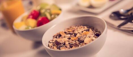 A breakfast setting with bowls of cereal and fruit, a glass of orange juice, and a plate with eggs.