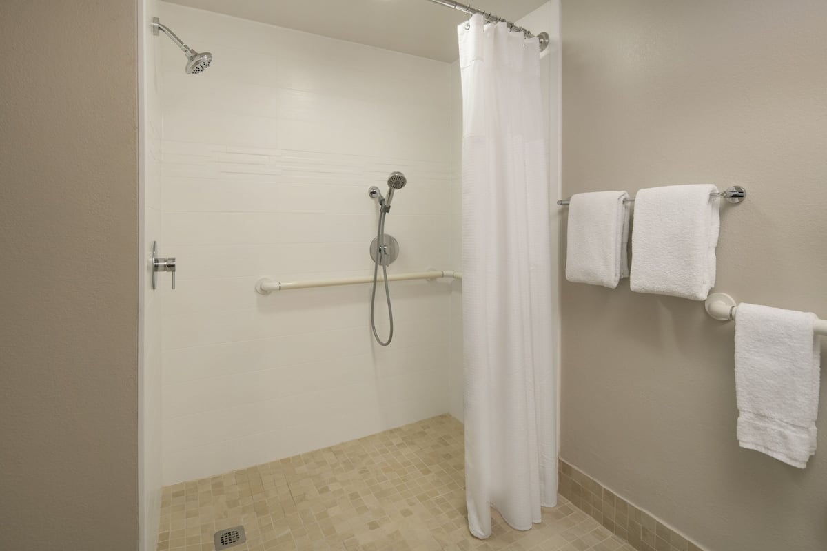 A bathroom with a shower, a toilet, and a towel rack with three towels.