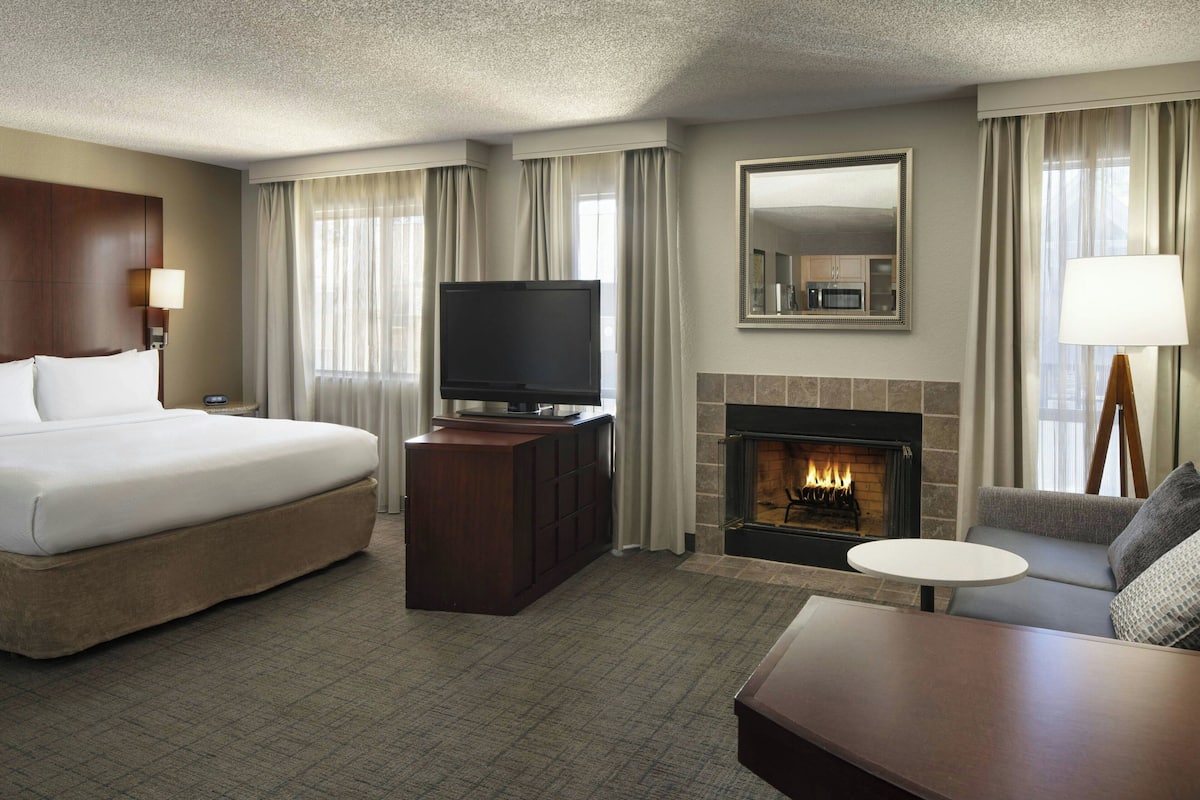 A hotel room with a large bed, a flat-screen TV, a fireplace, a sofa, and a small table.
