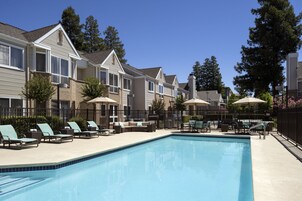 A swimming pool with lounge chairs and umbrellas, surrounded by multi-story buildings with a uniform architectural style.