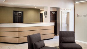 Un espace d’accueil avec un comptoir en bois, deux fauteuils et une porte portant l’inscription « The Market ».