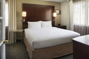 Quarto de hotel com uma cama grande, duas mesas de cabeceira e uma escrivaninha.