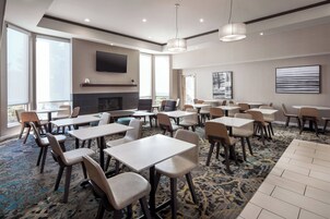 A spacious dining area with multiple tables and chairs, a fireplace, and large windows providing natural light.