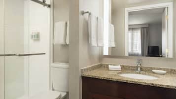 A modern bathroom with a glass shower enclosure, a white toilet, a granite countertop sink, and a dark wooden vanity.