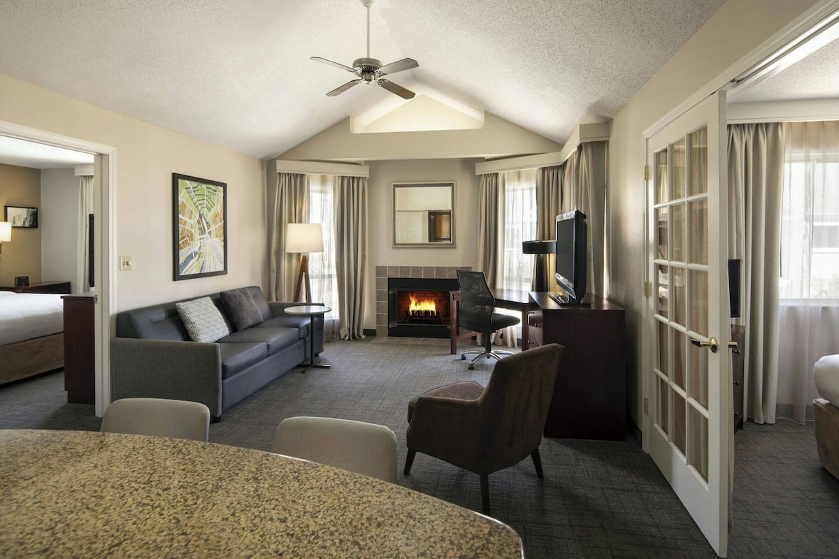 A hotel room with a fireplace, a sofa, a dining table, and a TV.