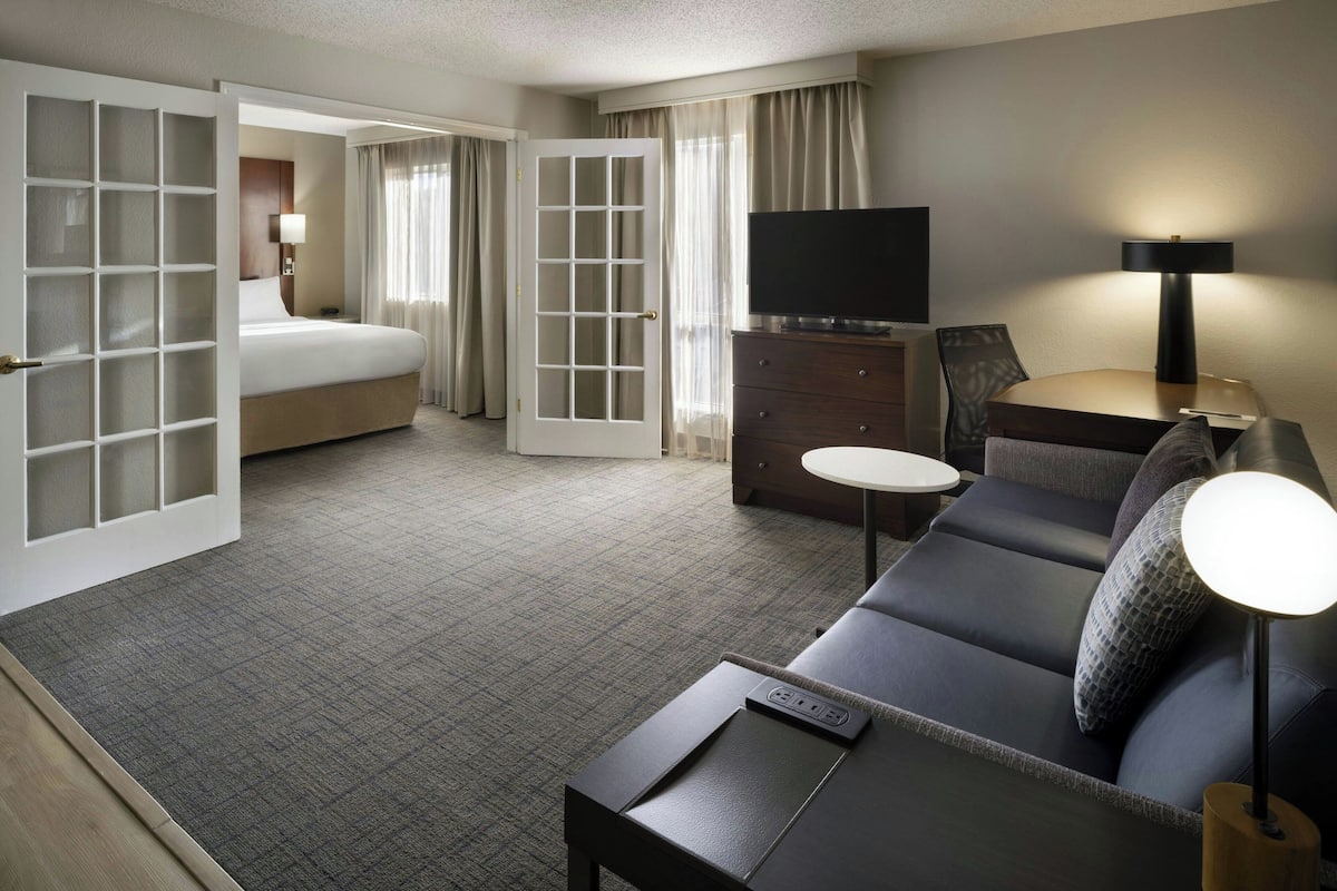 A hotel room with a bed, a sofa, a TV, a desk, and a lamp.