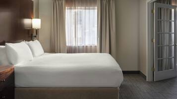 Habitación de hotel con una cama grande, una mesita de noche, una lámpara, una ventana con cortinas y una puerta.