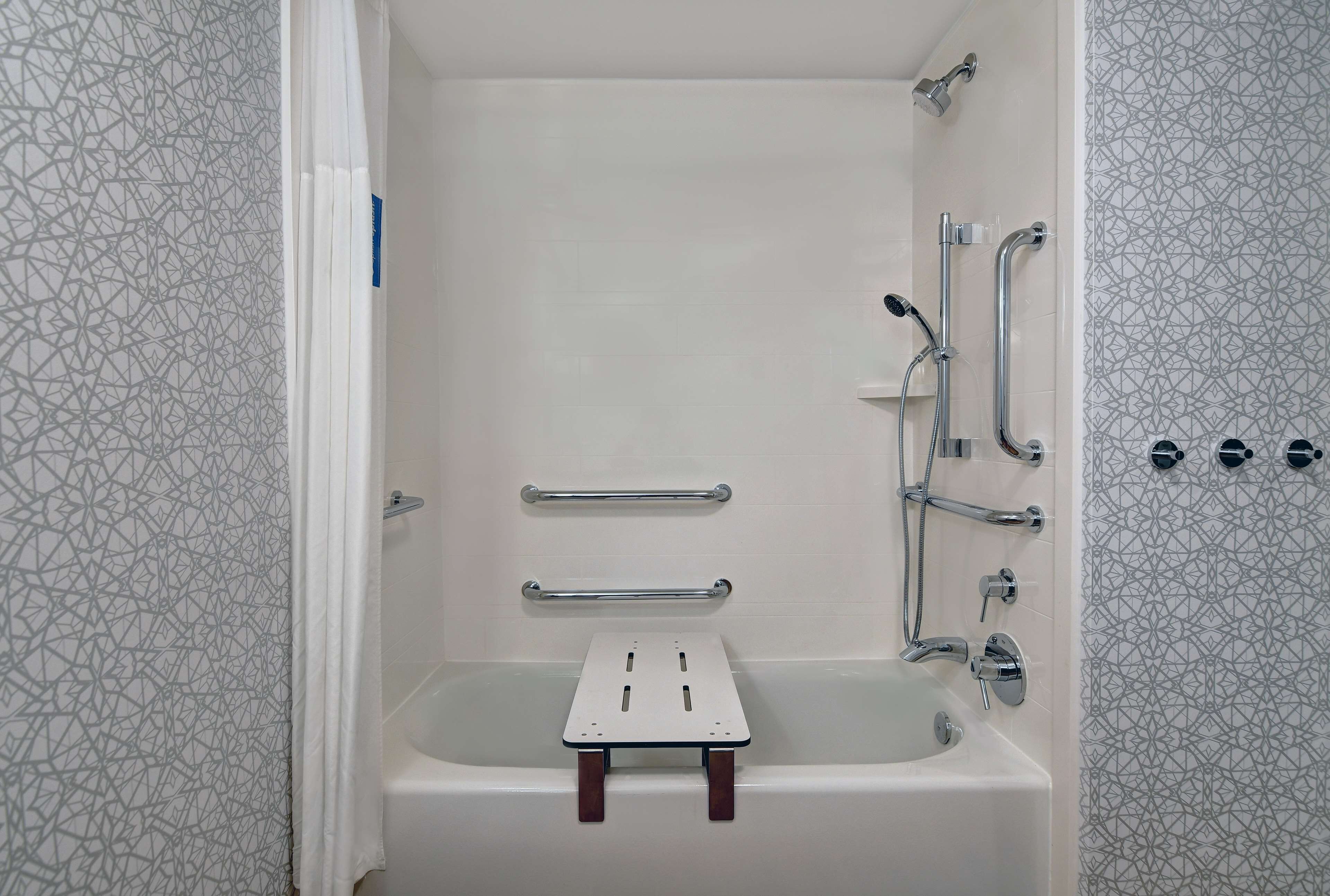 A bathroom with a bathtub, grab bars, and a showerhead.