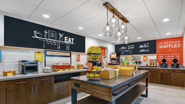 A modern kitchen with a central island, a chalkboard menu, and a sign promoting waffles. - Hampton Inn Charleston/Mount Pleasant-Patriots Point (Mount Pleasant)