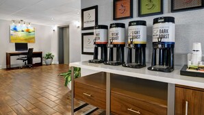 A coffee station with four dispensers labeled 'Hot Water,' 'Decaf Roast,' 'Light Roast,' and 'Dark Roast.' There are framed artworks on the wall and a desk with a computer and chair. - Hampton Inn Charleston/Mount Pleasant-Patriots Point (Mount Pleasant)