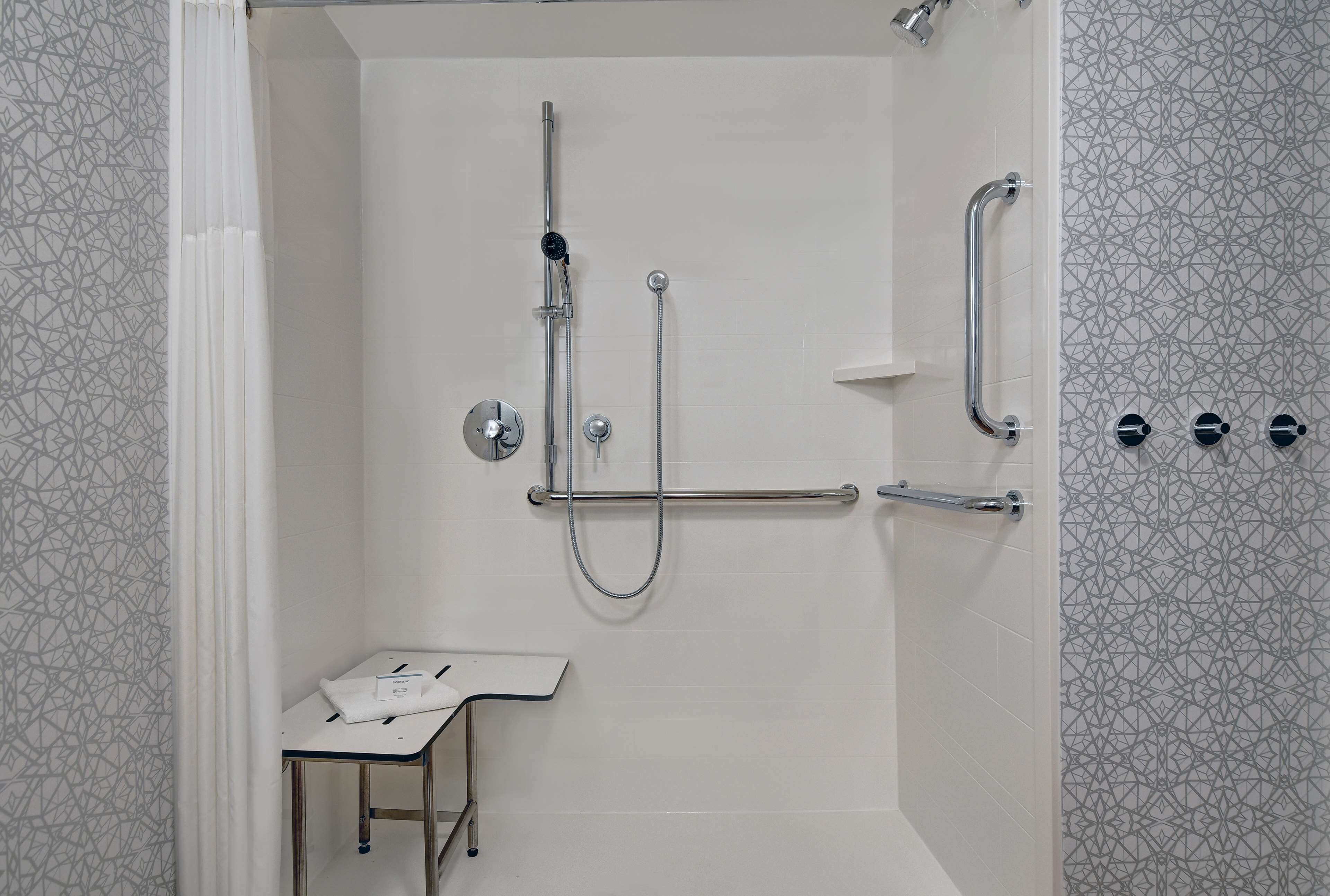 A shower area with a handheld showerhead, a wall-mounted faucet, and a grab bar.