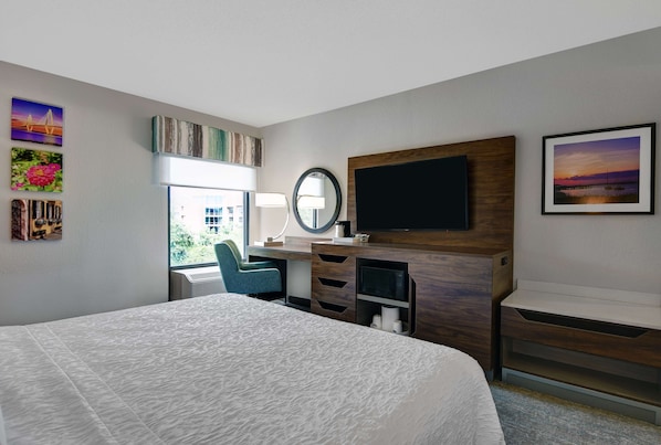 A hotel room with a large bed, a desk with a chair, a TV, and artwork on the walls.