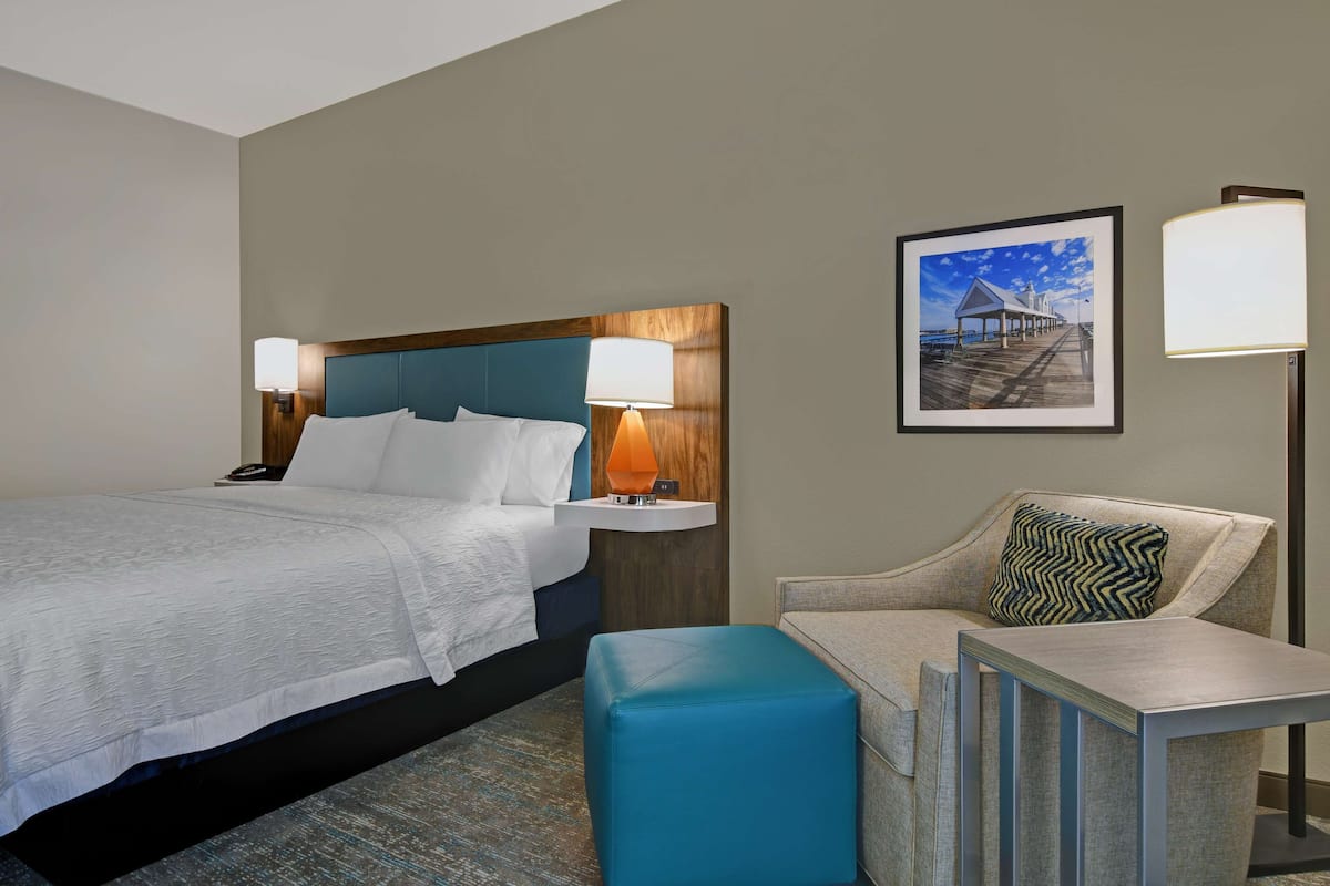A hotel room with a bed, a nightstand, a desk, a chair, and a picture on the wall.