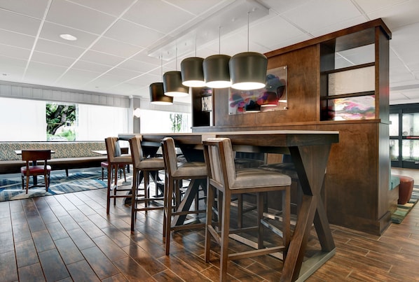 Een moderne bar met houten barstoelen, hangende verlichting en een groot raam met uitzicht op de omgeving.