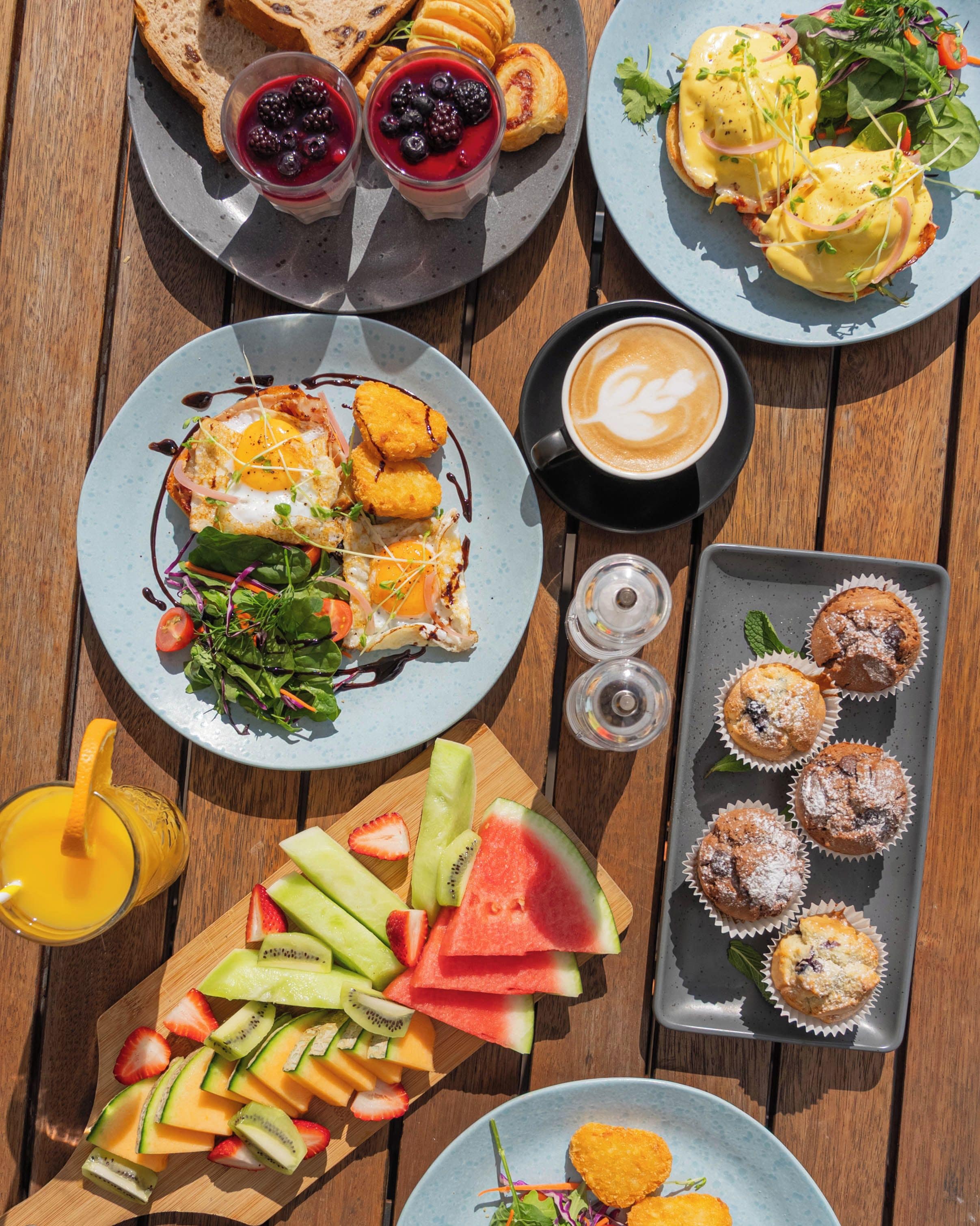 A variety of breakfast items including toast, fruit, muffins, and coffee on a wooden table.