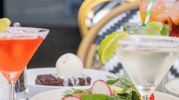A table with various dishes including a salad, pasta, and appetizers, along with two cocktails.