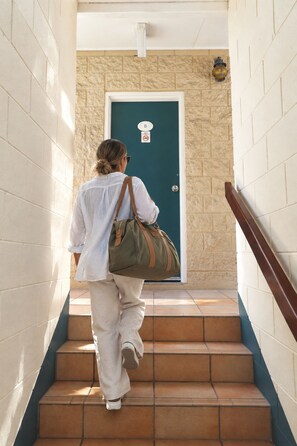 Una persona bajando una escalera que tiene una puerta al final, un aplique en la pared y un cartel con el número de la puerta.