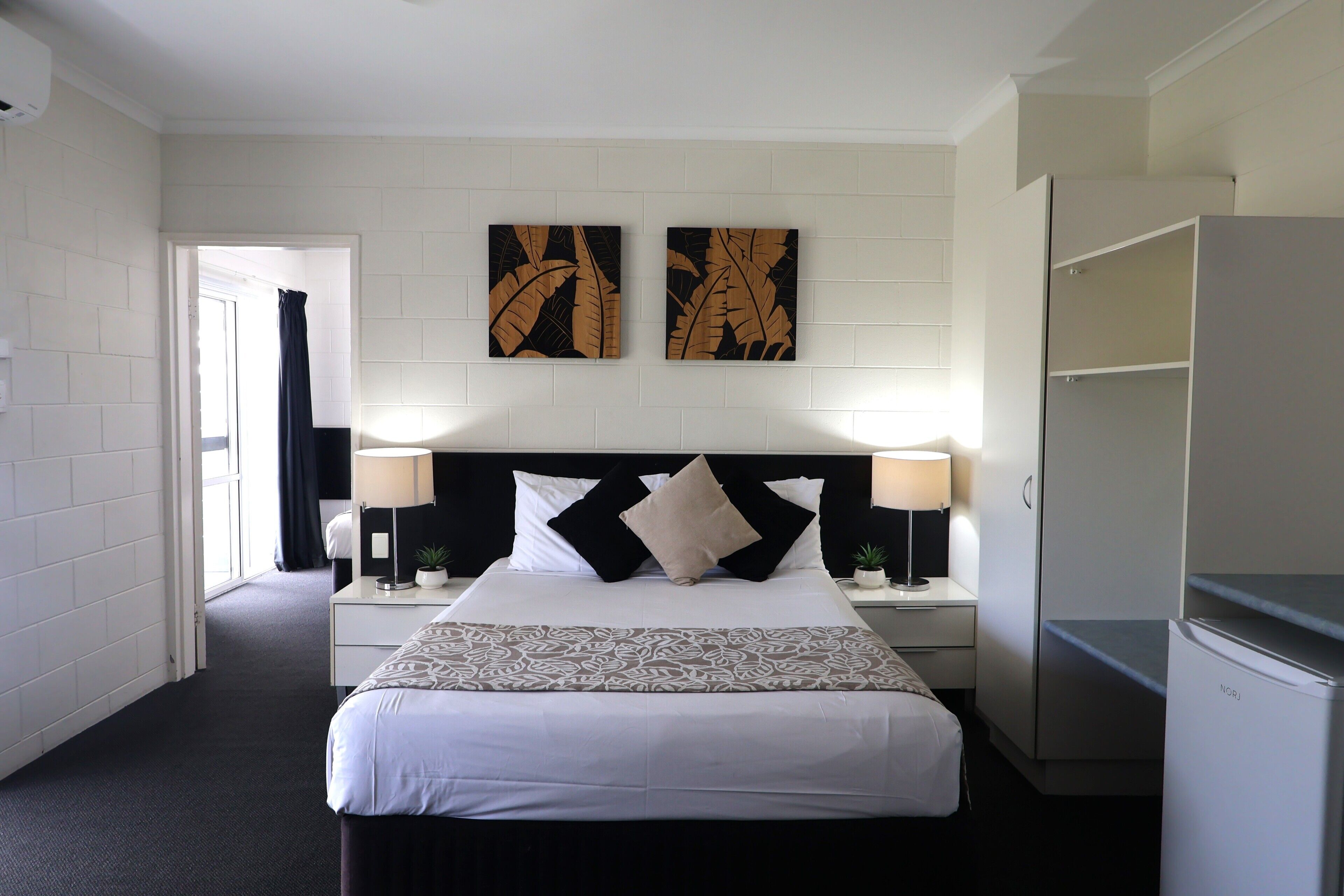Une chambre d’hôtel comprenant un lit, deux tables de chevet, un bureau, une armoire et des œuvres d’art accrochées au mur.