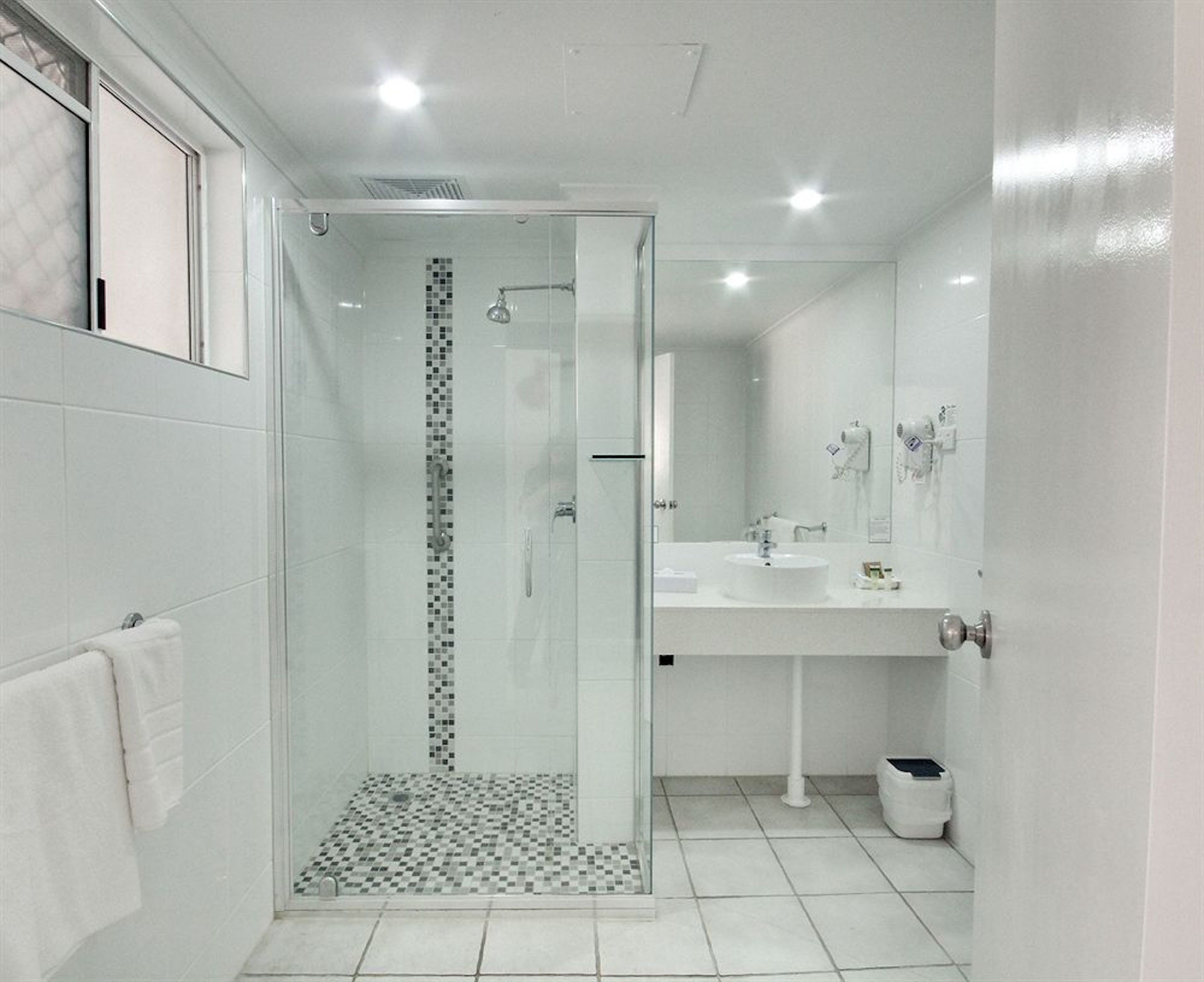 Un baño moderno con ducha envuelta en vidrio, un lavabo blanco y un espejo.
