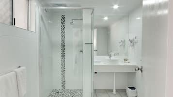 Un baño moderno con ducha envuelta en vidrio, un lavabo blanco y un espejo.