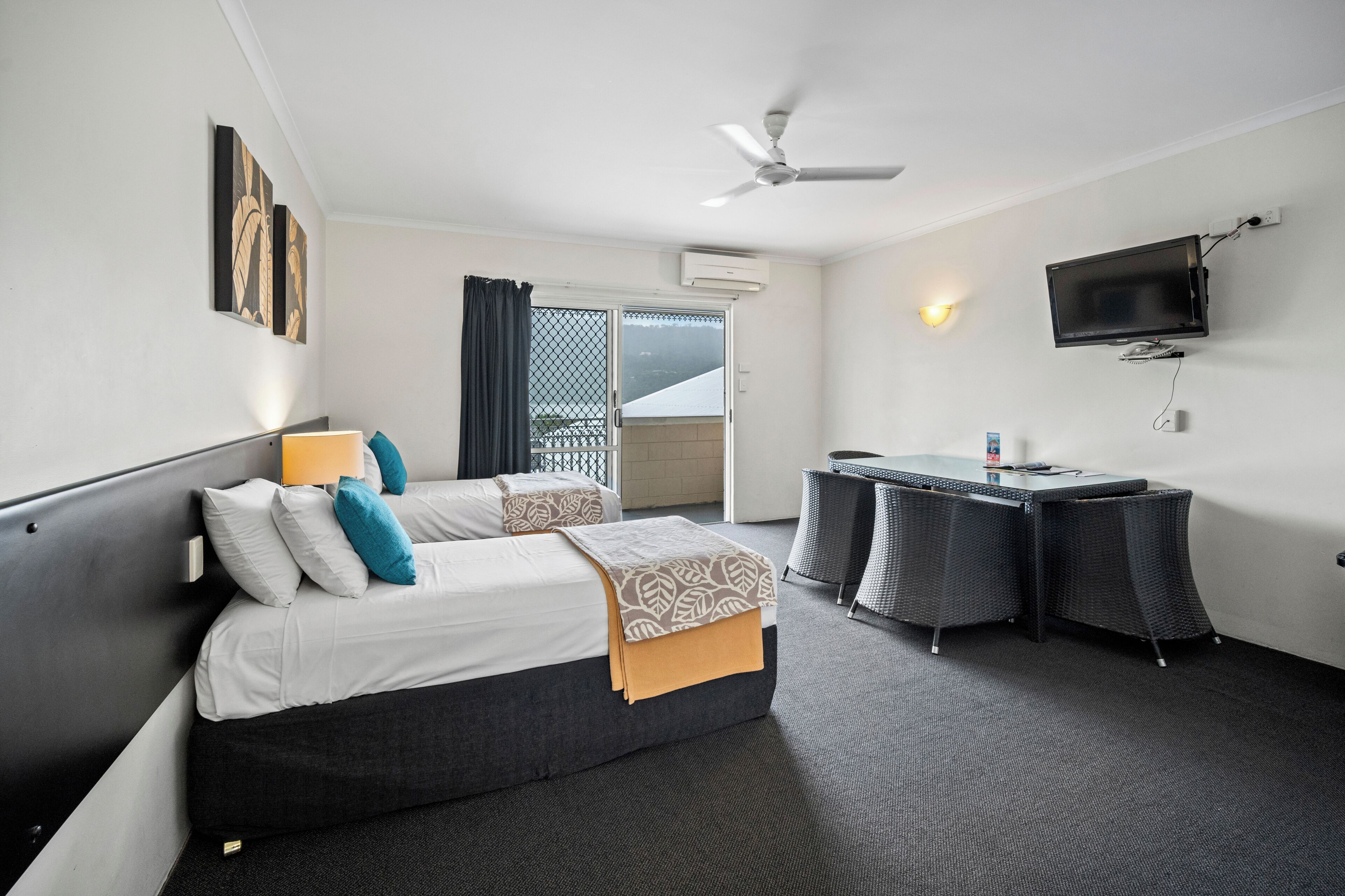A hotel room with two beds, a desk, a television, and a balcony.