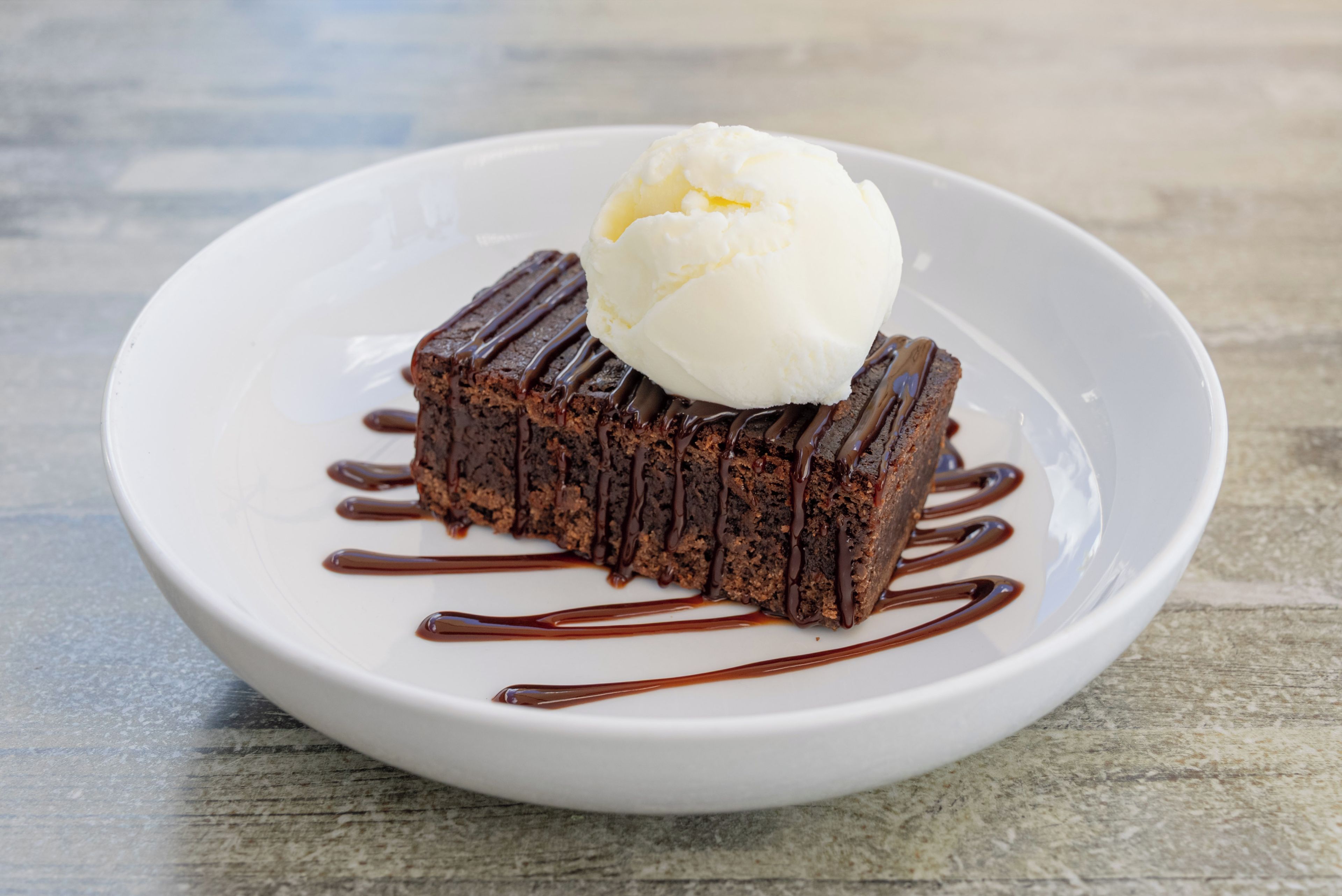 Een dessert op een wit bord, met chocoladesaus en een bol ijs.