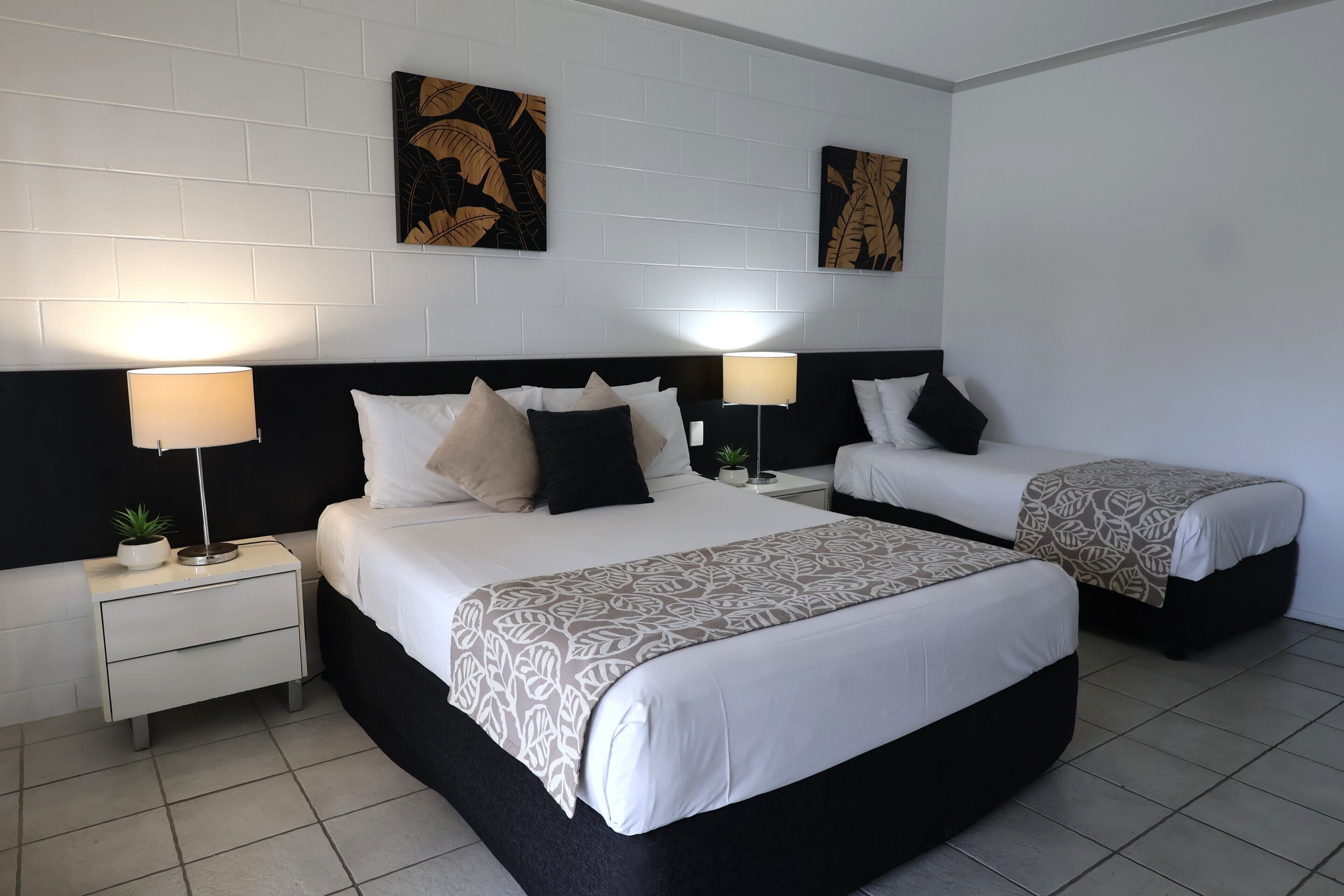 Ein Hotelzimmer mit einem großen Bett, zwei Nachttischen, zwei Lampen und zwei an der Wand befestigten Kunstwerken.