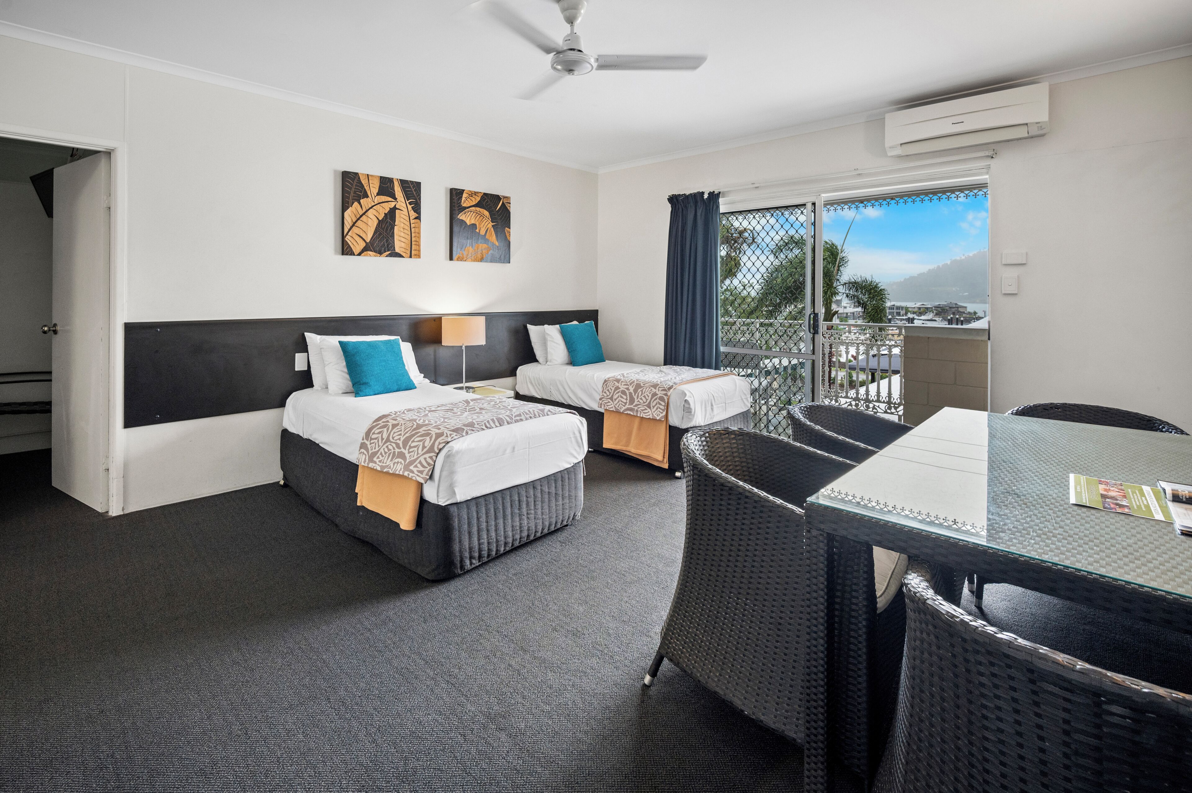 A hotel room with two beds, a dining table, a ceiling fan, and a view of the outdoors.