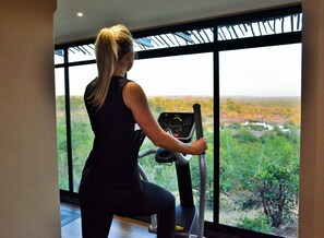 A woman exercising on a treadmill with a view of a landscape through large windows.