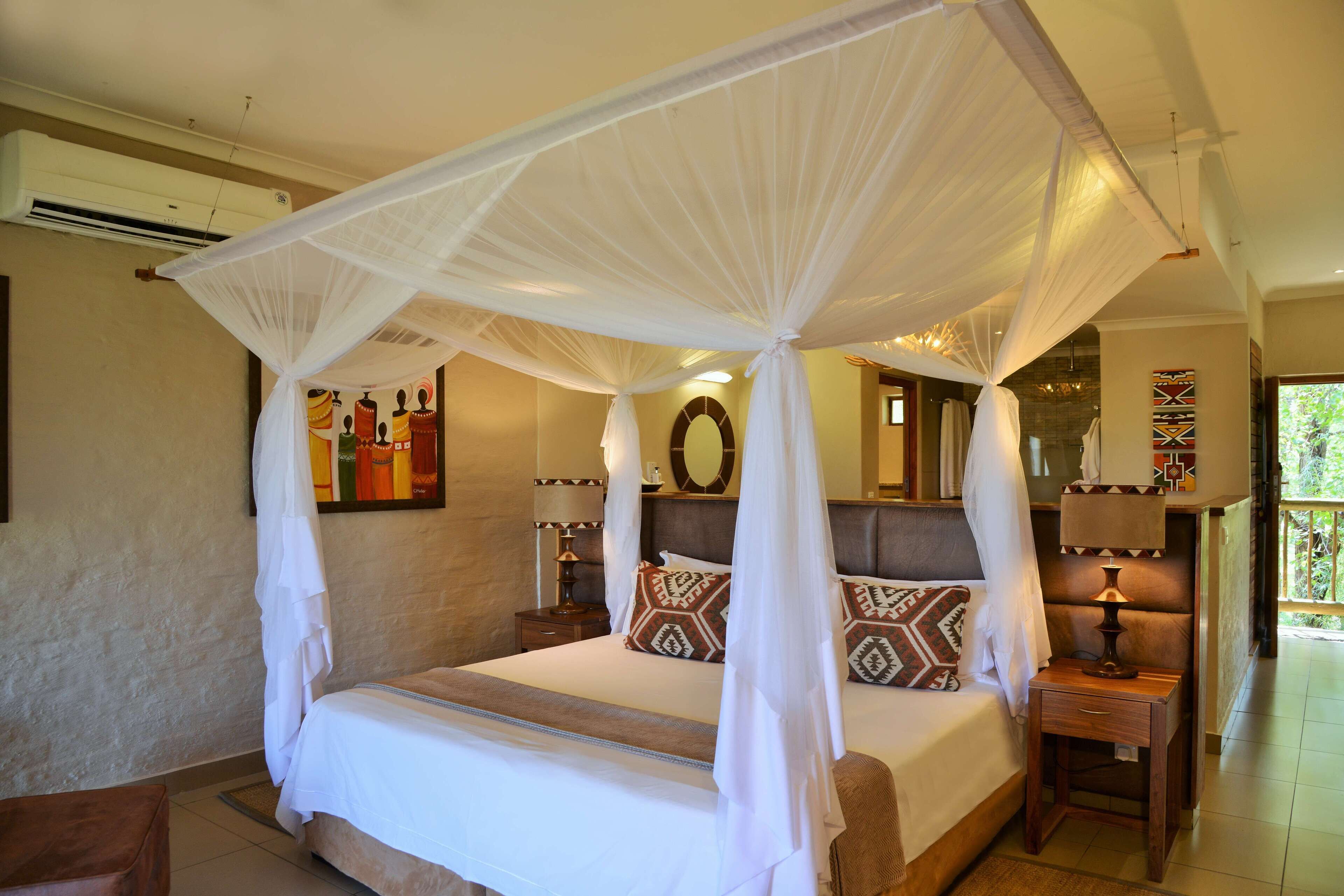 A four-poster canopy bed with a headboard, bedside tables with lamps, and artwork on the walls.