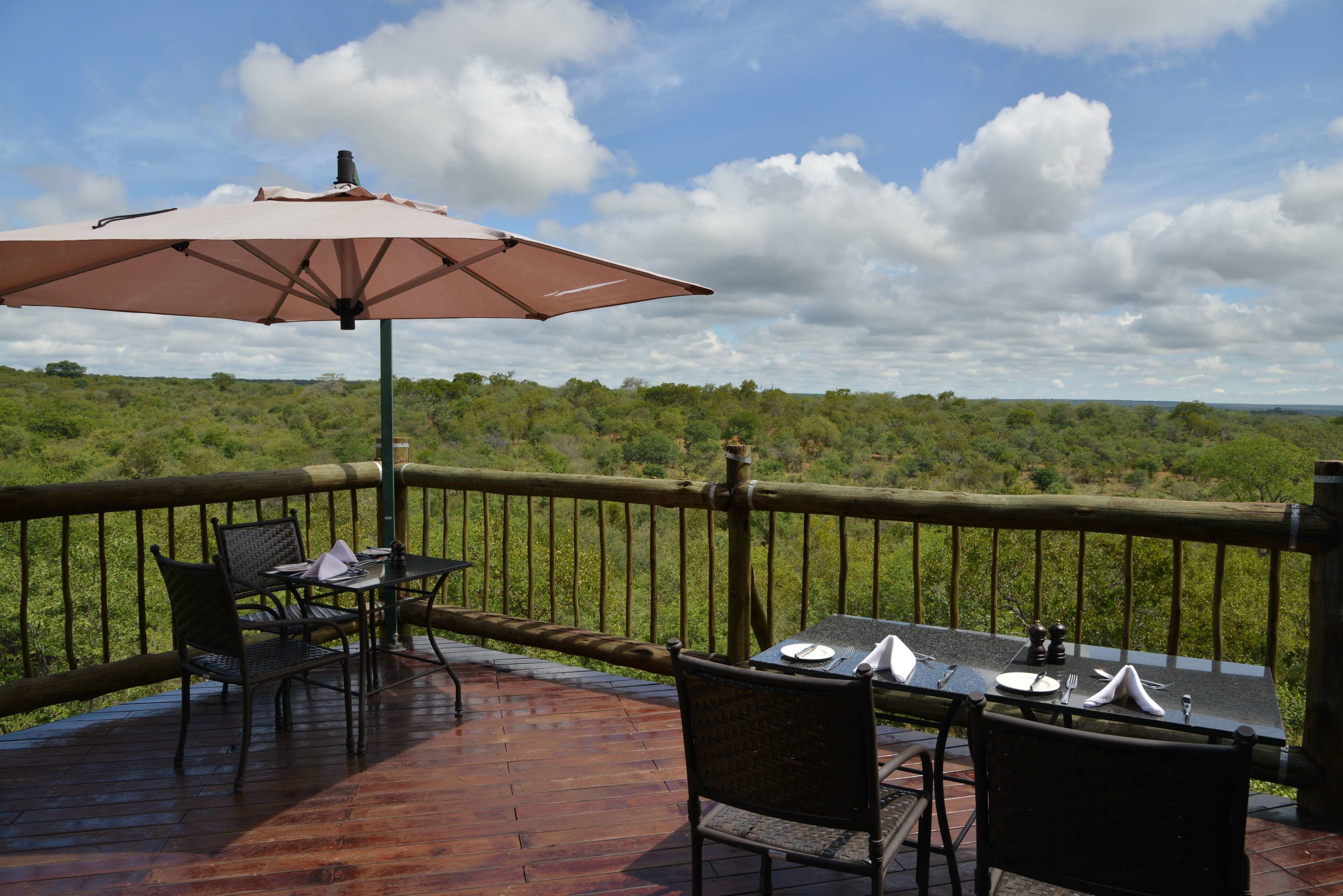 A wooden deck with a table and chairs, an umbrella, and a view of a green landscape.