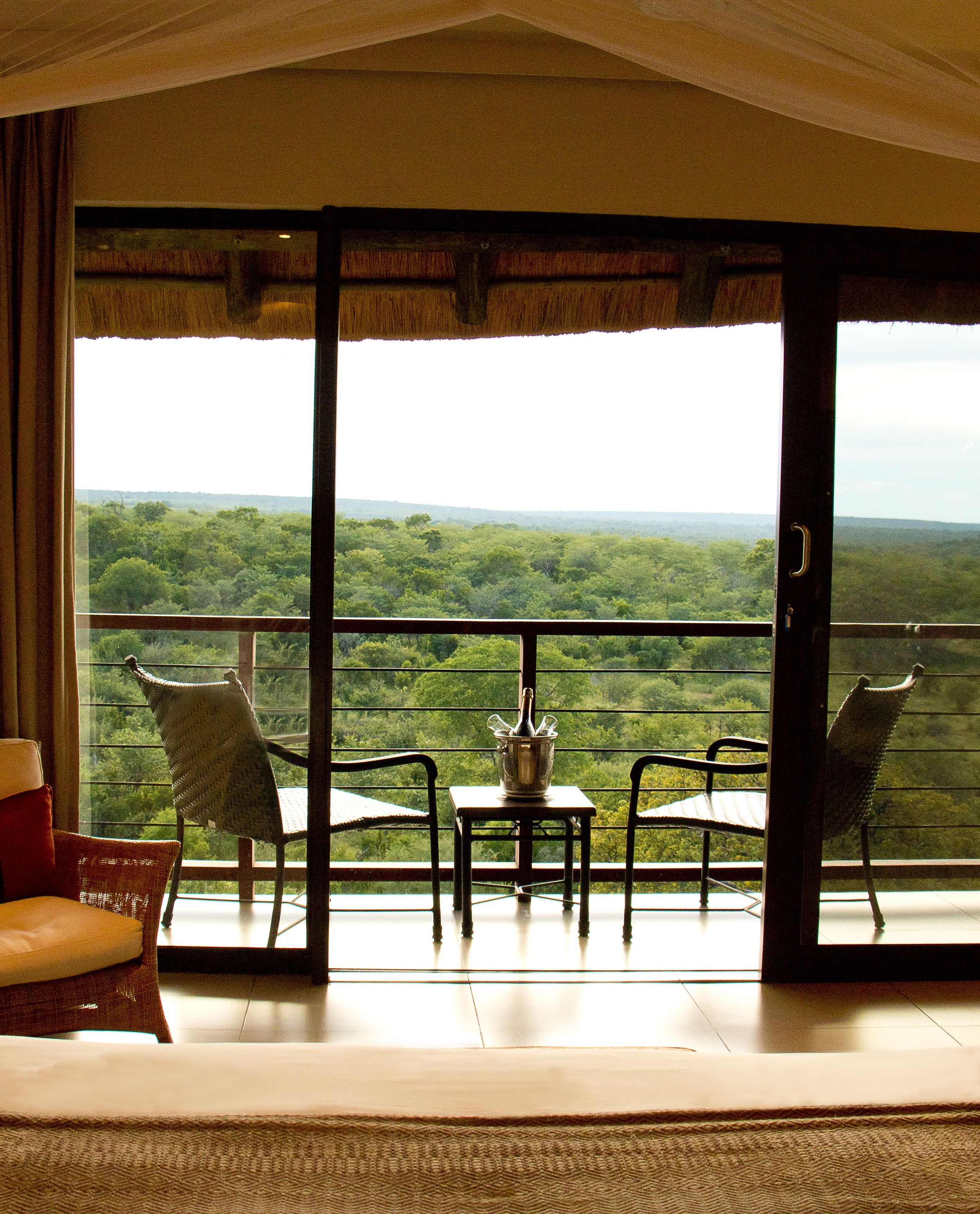 Un balcón con sillas de mimbre y una mesa, con vistas a un exuberante paisaje verde.