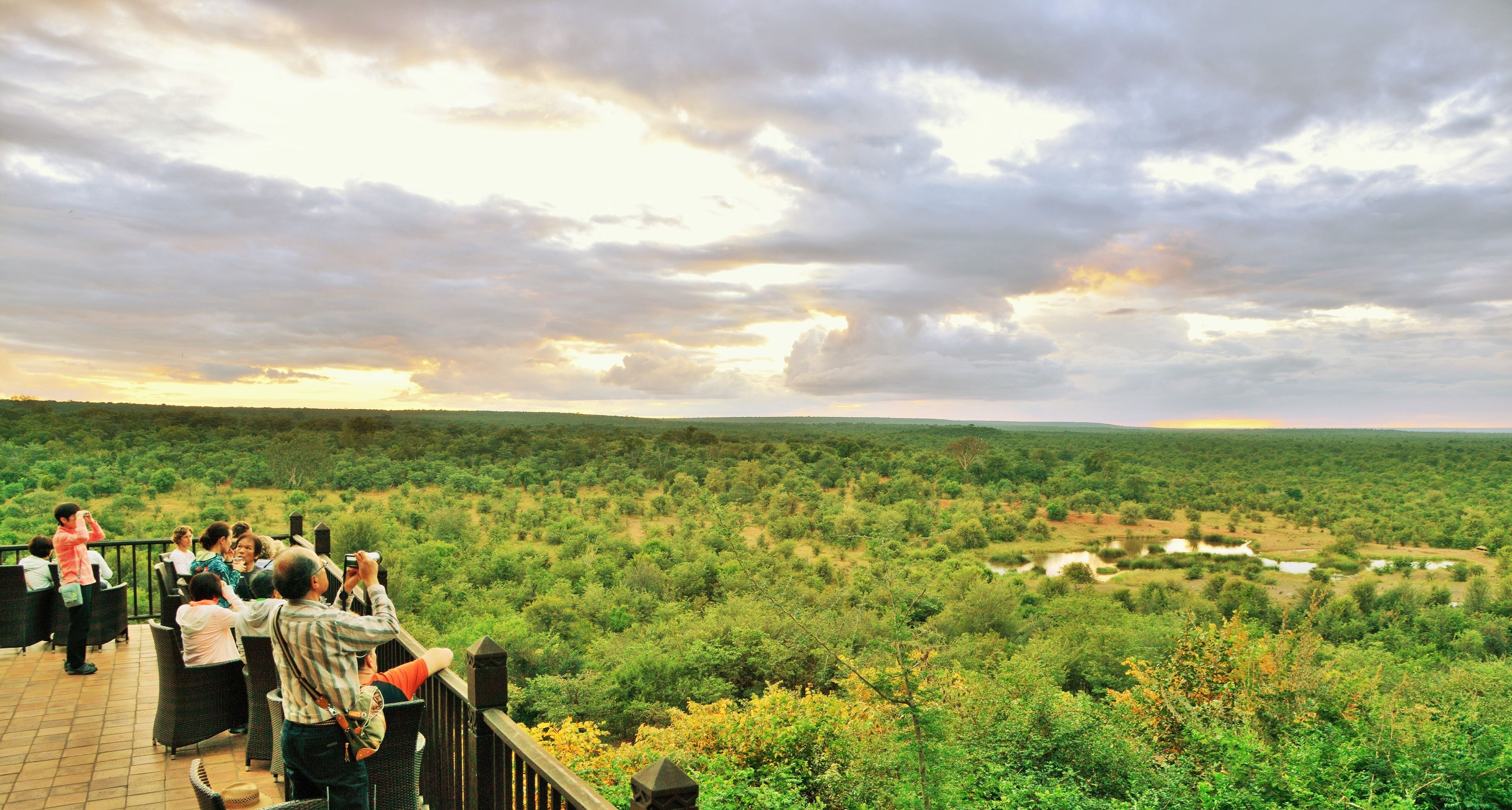 A terrace with a view of a lush landscape and a group of people taking photos.