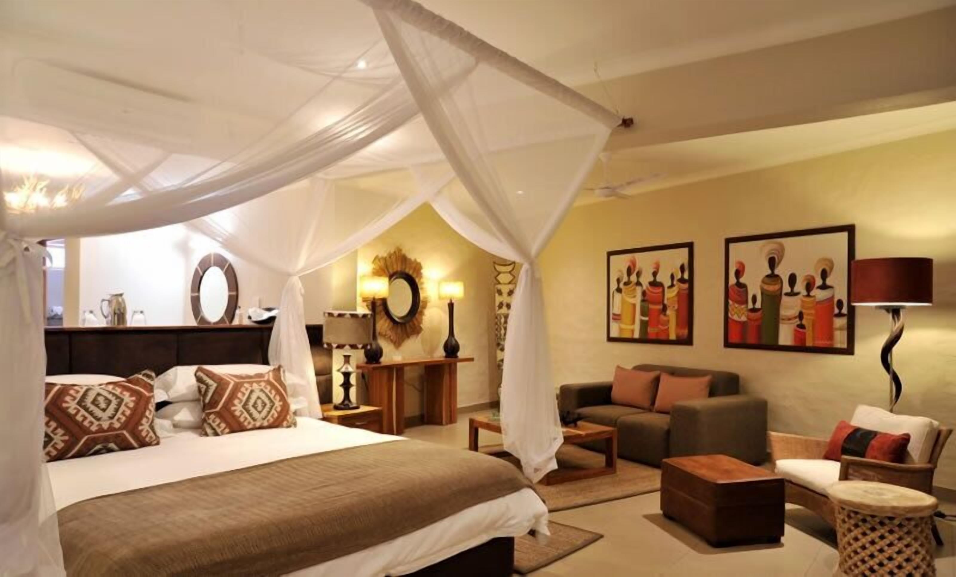 A bedroom with a canopy bed, a sitting area with a sofa and armchairs, and artwork on the walls.
