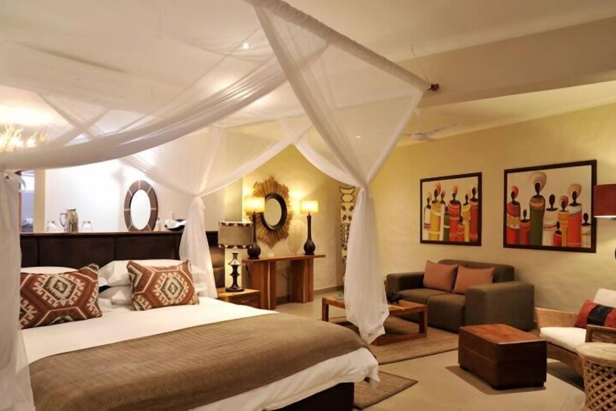 A bedroom with a canopy bed, a sofa, a coffee table, and artwork on the walls.
