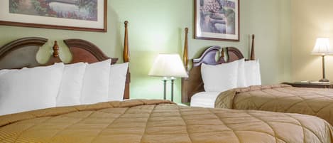 A hotel room with two queen beds, a nightstand with a lamp, and two framed paintings on the wall.