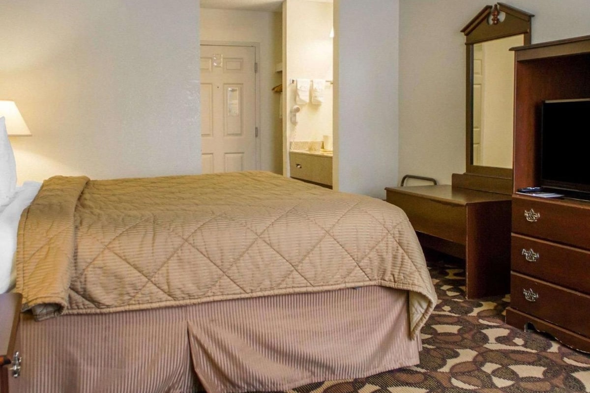 A hotel room with a bed, a dresser, a mirror, and a television.