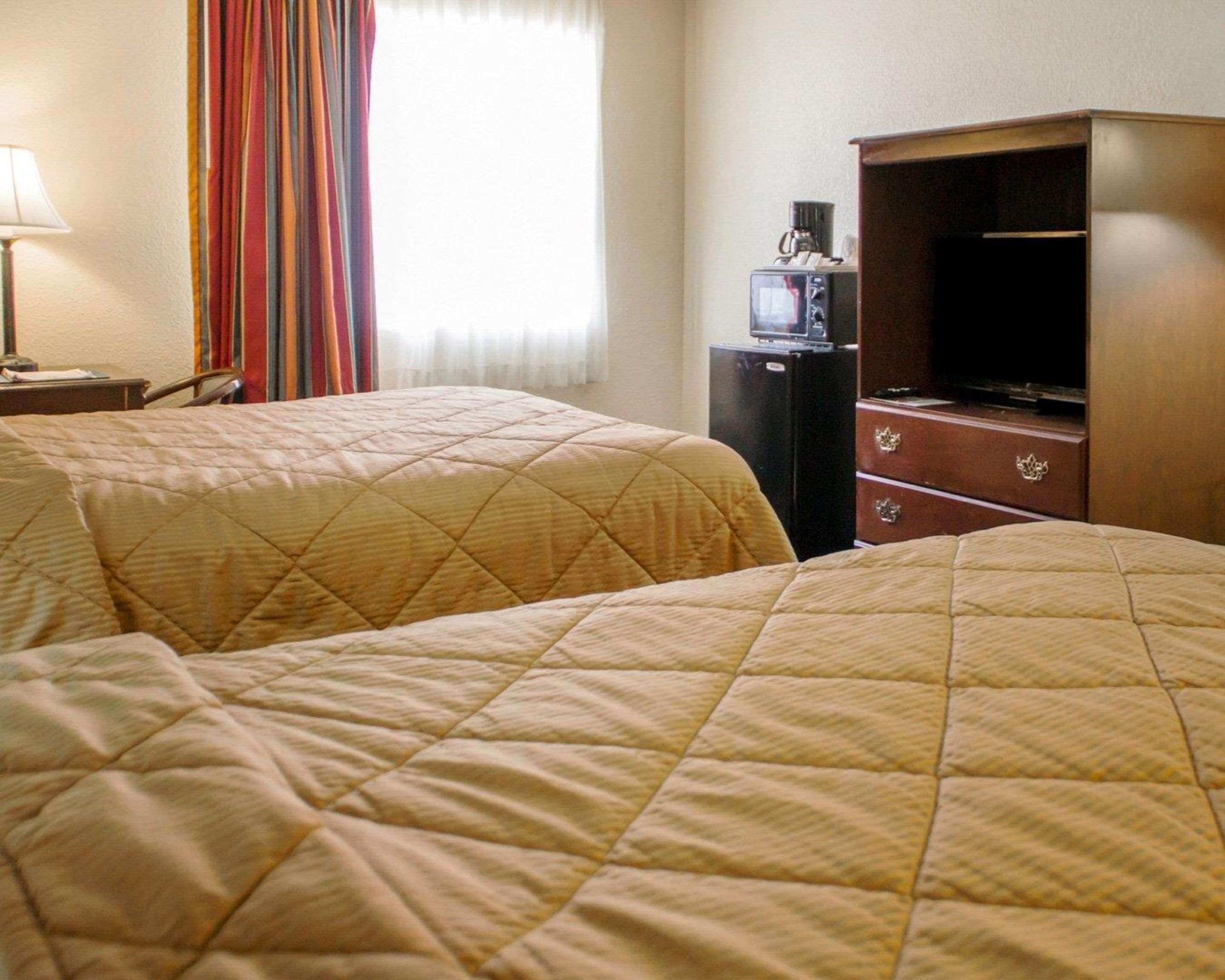 A hotel room with two beds, a television on a wooden cabinet, and a lamp on a side table.
