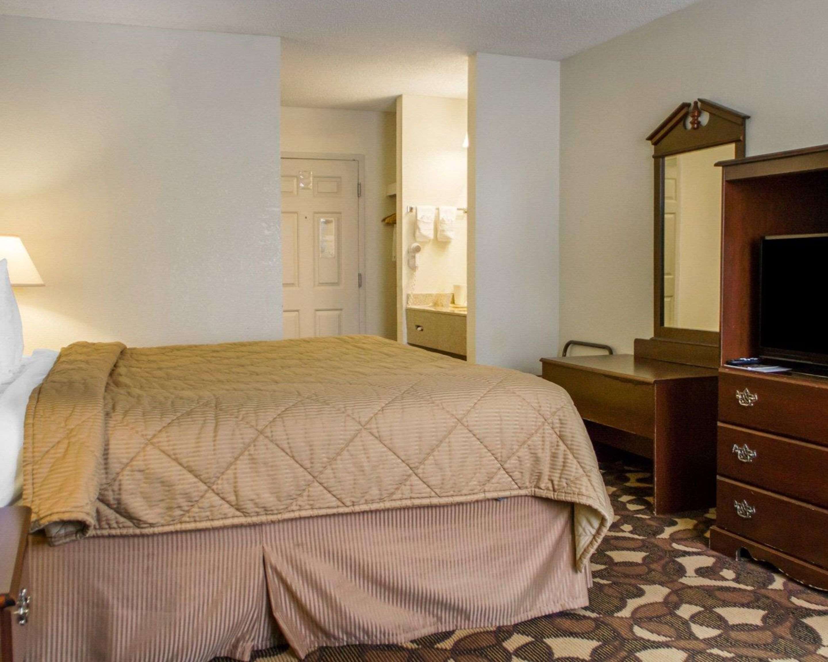 A hotel room with a bed, a dresser, a mirror, and a desk.